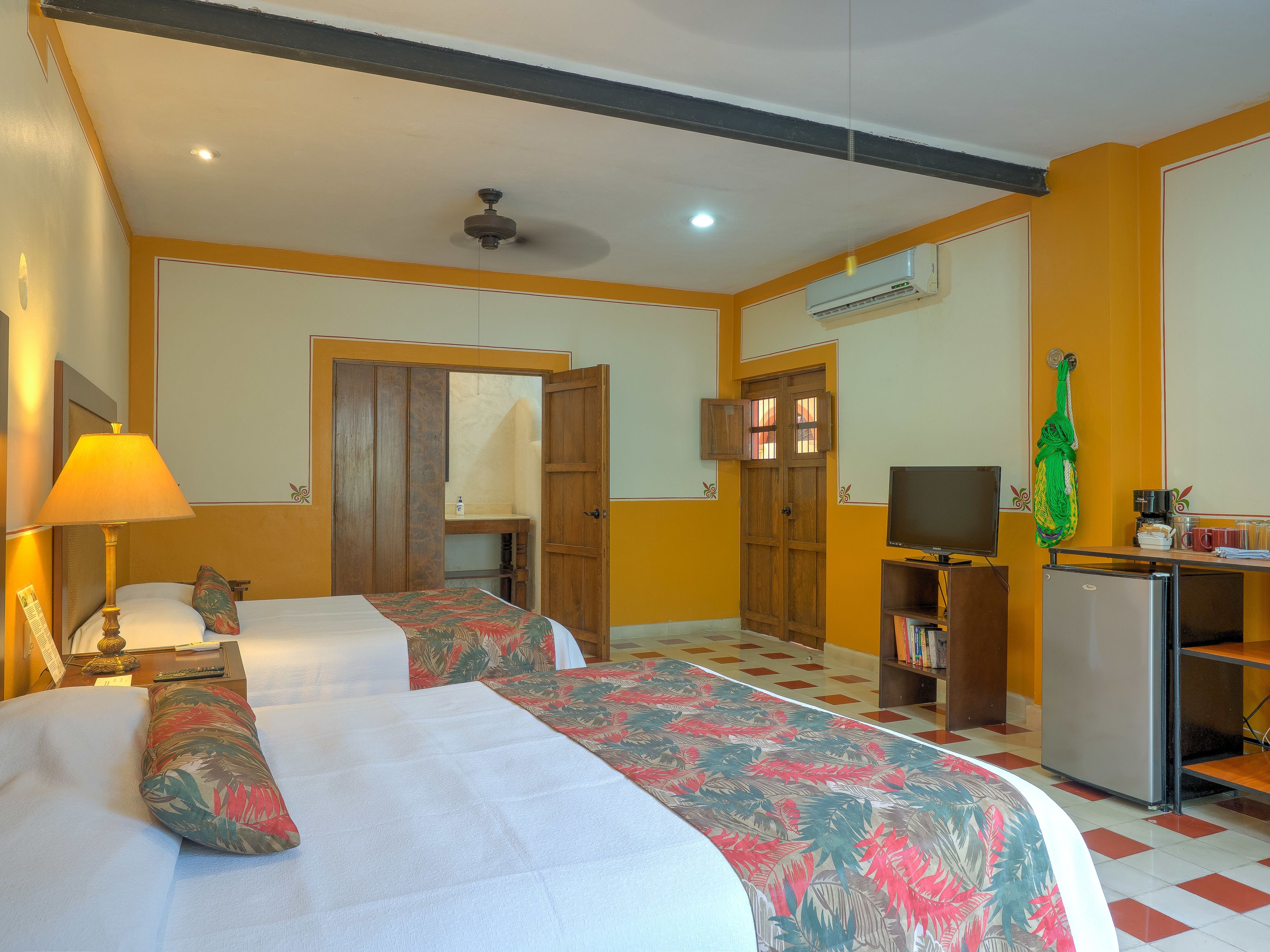 Una habitación de hotel con dos camas, un escritorio con televisor, aire acondicionado y un armario.