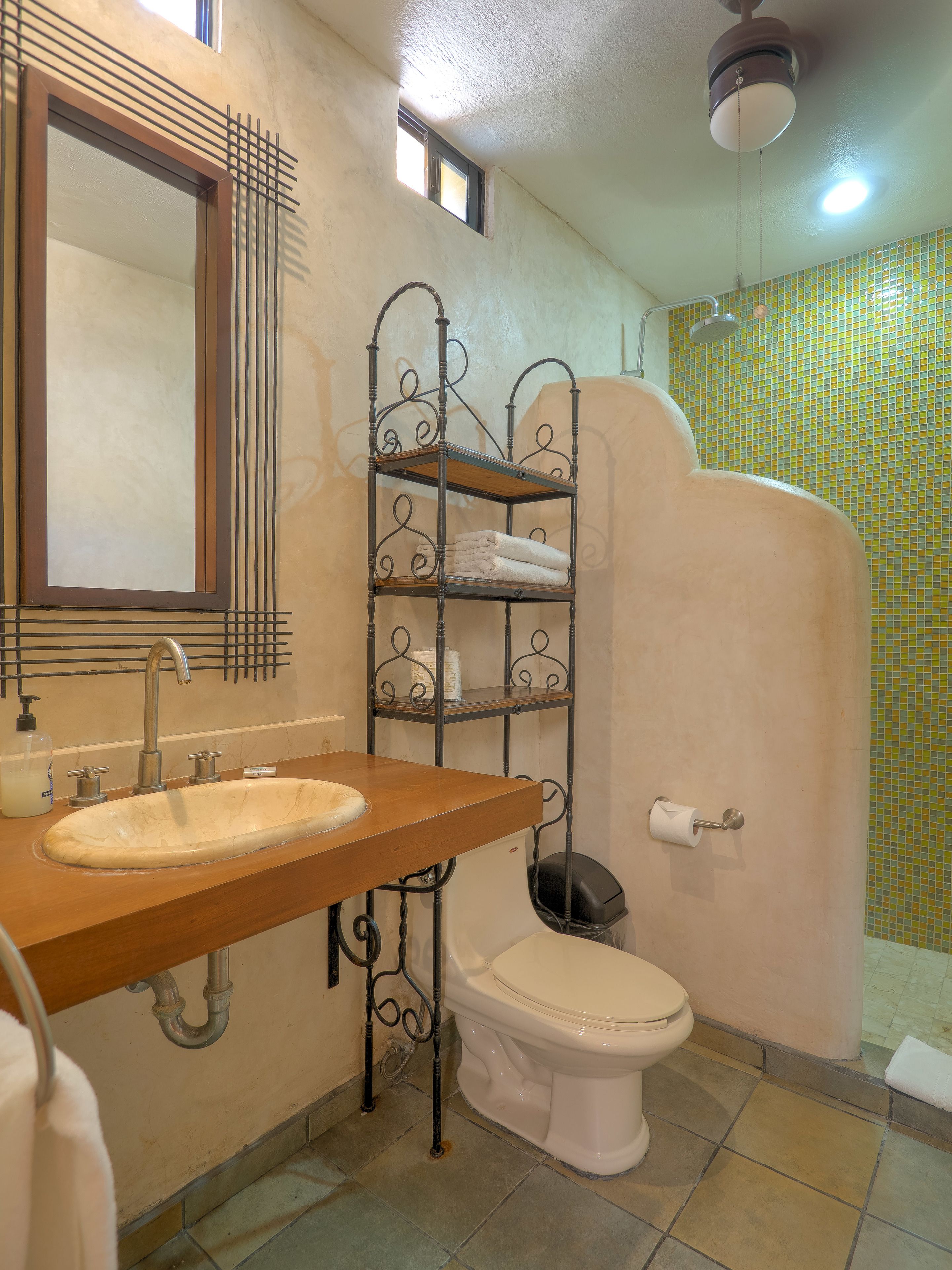 Un baño con tocador de madera, inodoro y estante metálico.