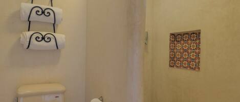 A bathroom with a toilet, a towel rack with three towels, a shower door, and a small window.