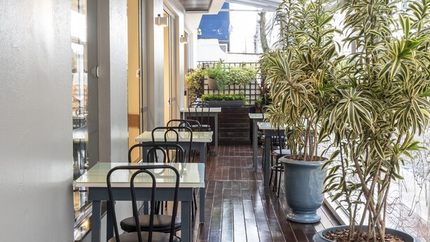 A covered outdoor dining area with tables and chairs, potted plants, and a view of the street. - Hotel Negrini (Balneário Camboriú)