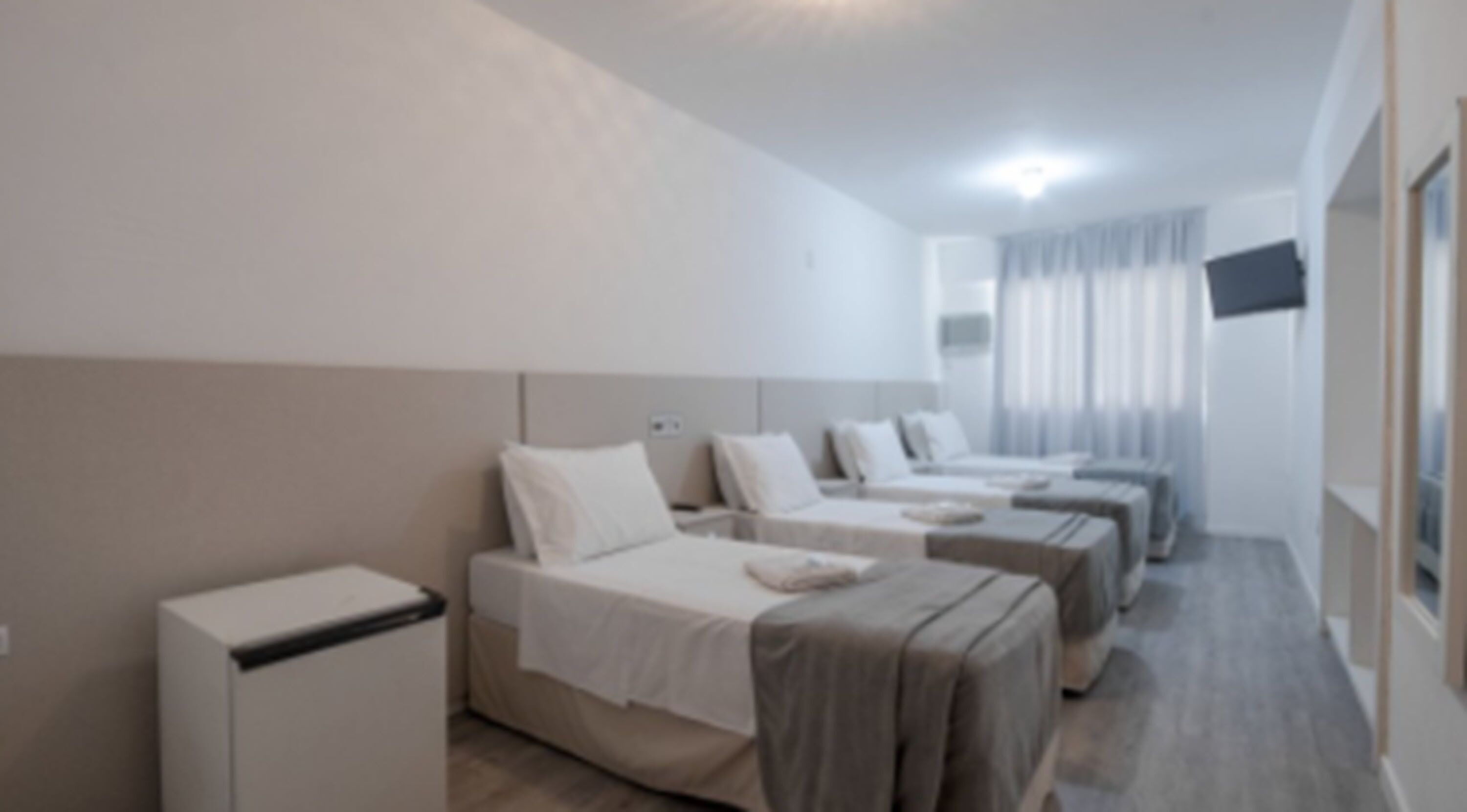 Una habitación de hotel con tres camas individuales, una mesita de noche pequeña y un televisor montado en la pared.