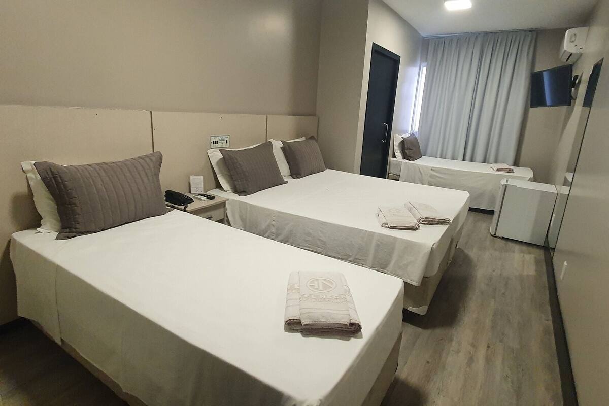 A hotel room with two single beds, a bedside table with a lamp, a mirror, and a window with curtains.