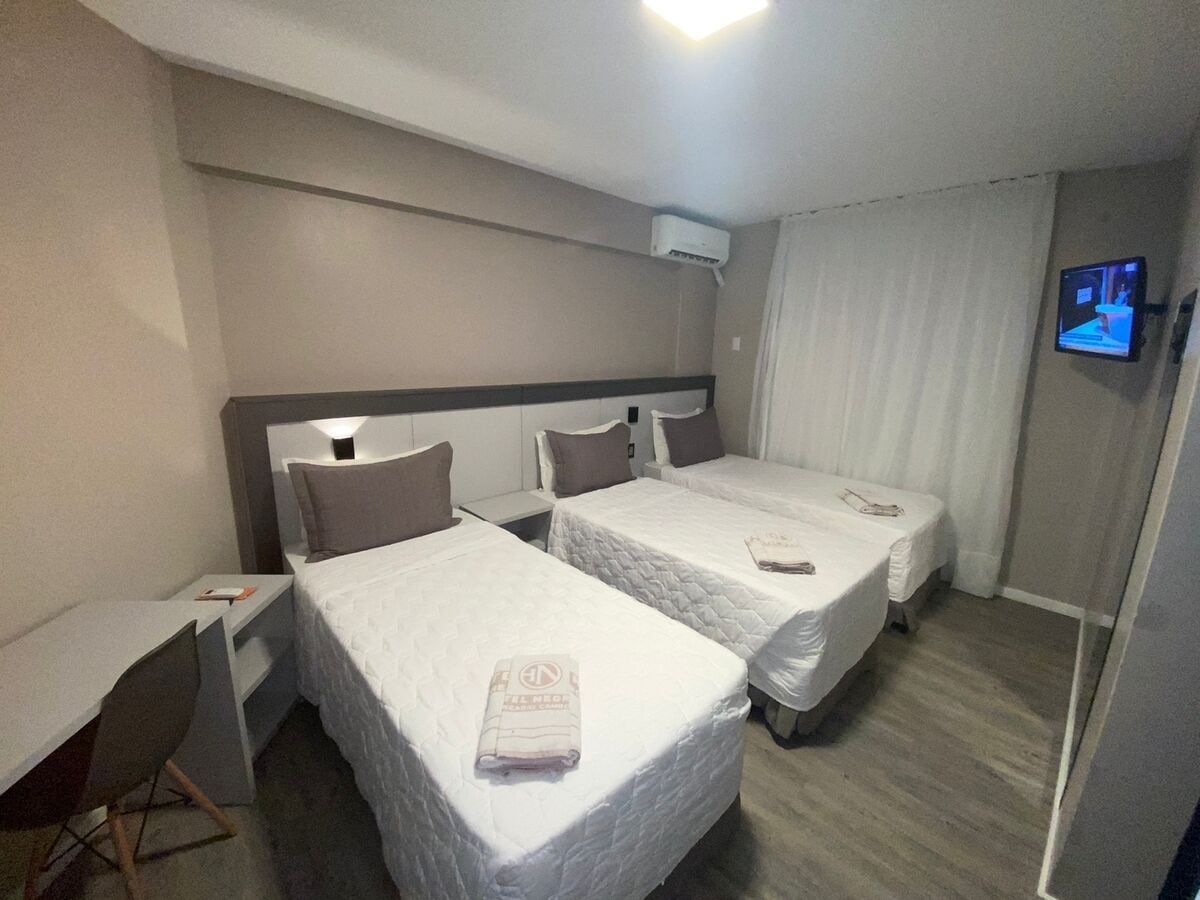 A hotel room with two single beds, a desk, a chair, and a TV mounted on the wall.