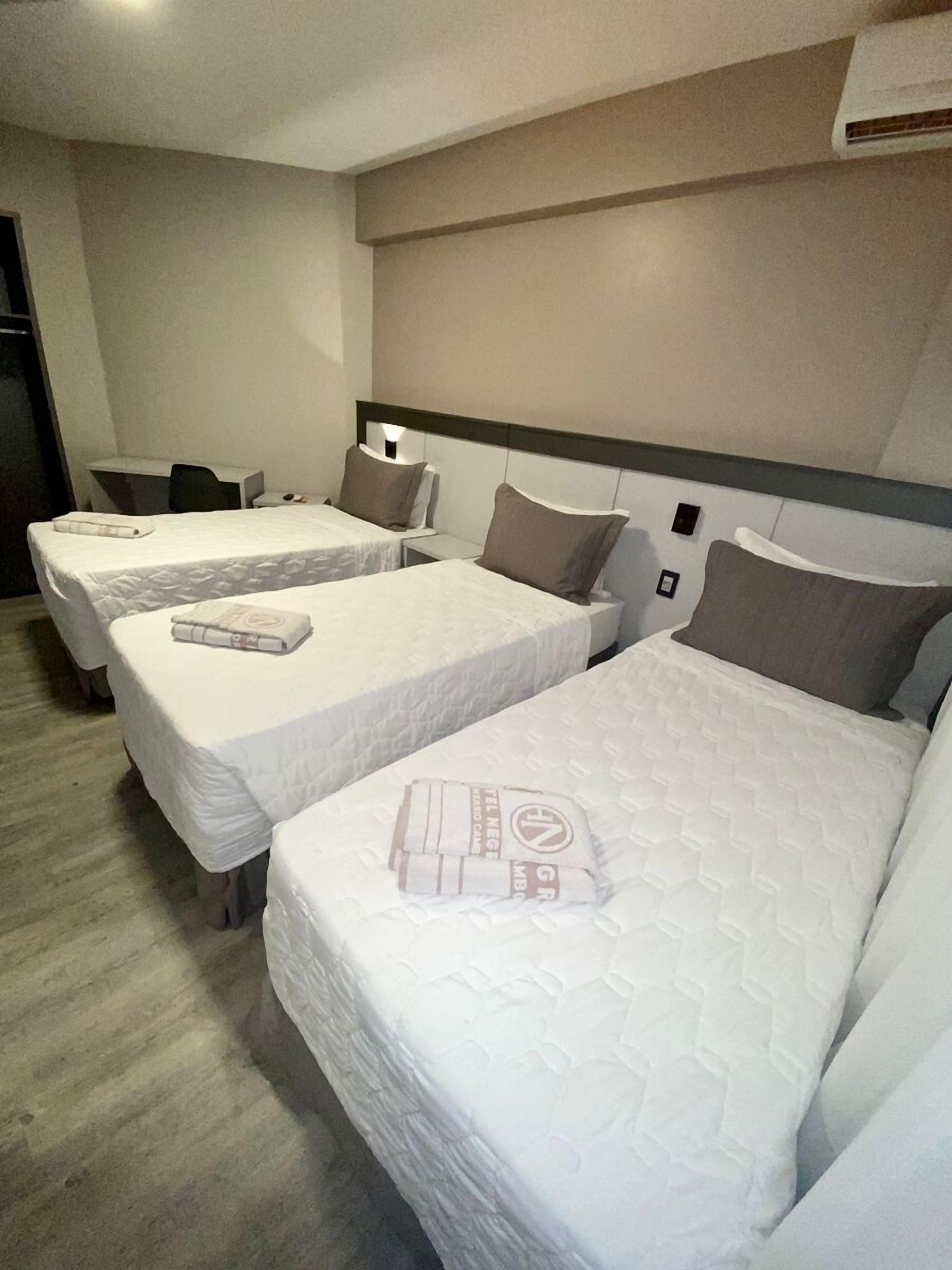 Une chambre d’hôtel avec deux lits simples, chacun étant équipé d’un oreiller et d’une serviette pliée. On y trouve un bureau avec une chaise et une petite table.