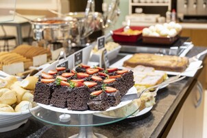 Un bufé con diversos postres, incluyendo pastel de chocolate con fresas, pan y otras preparaciones horneadas.