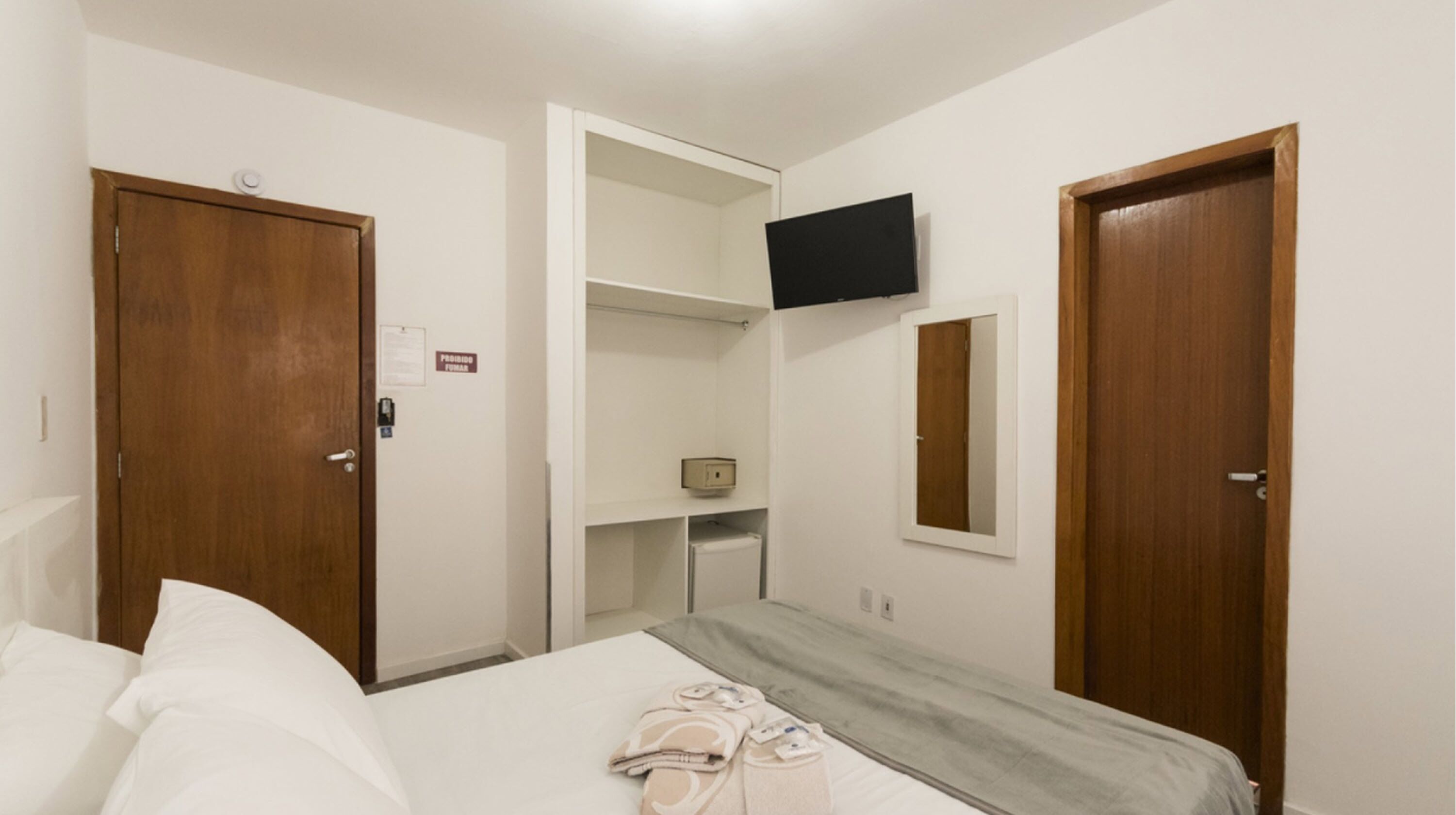 Ein Hotelzimmer mit einem Bett, einem an der Wand befestigten Fernseher und einer Holztür.