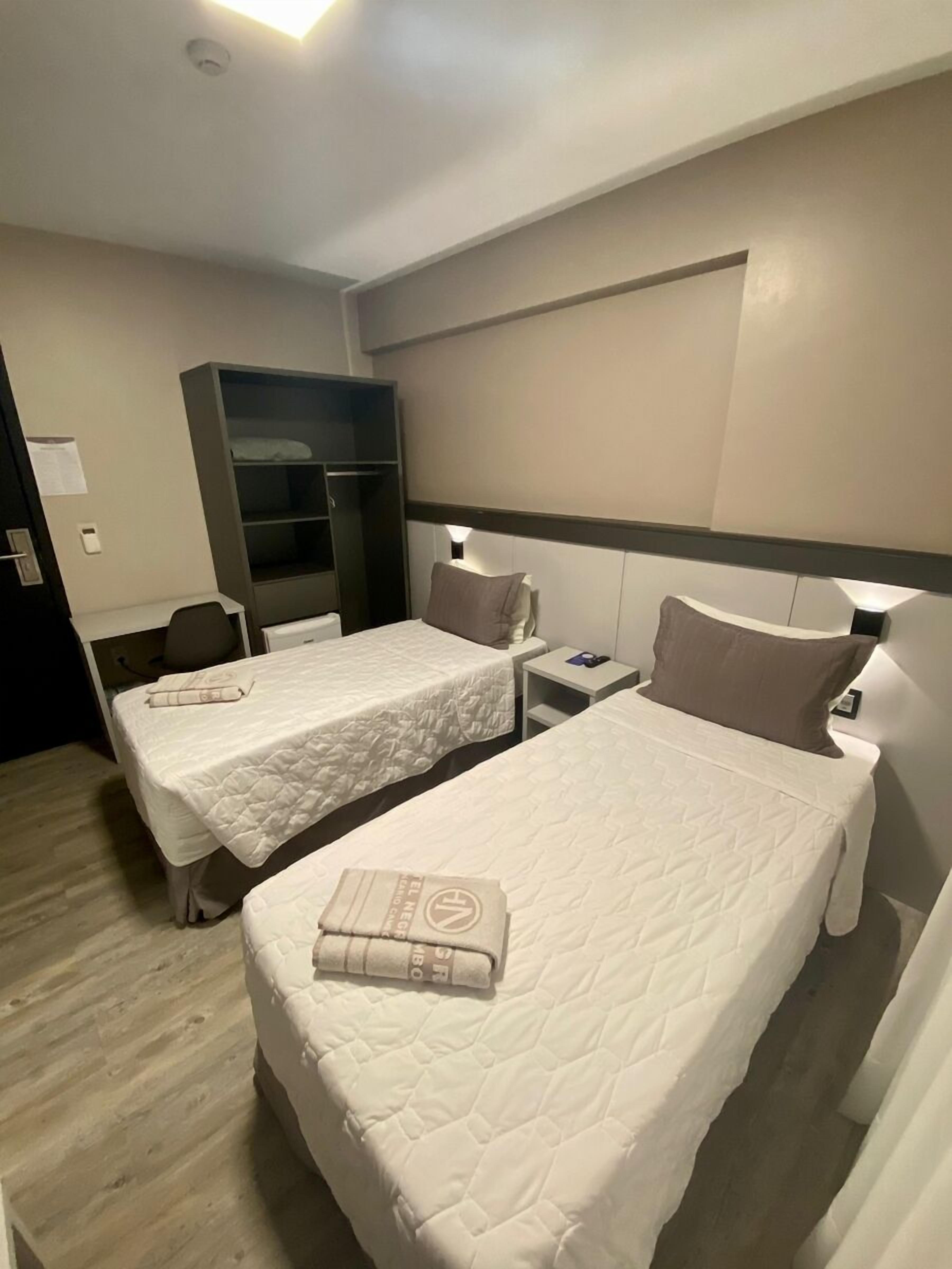 A hotel room with two single beds, a wardrobe, a desk, and a chair.