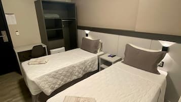Una habitación de hotel con dos camas individuales, un armario, un escritorio y una silla.