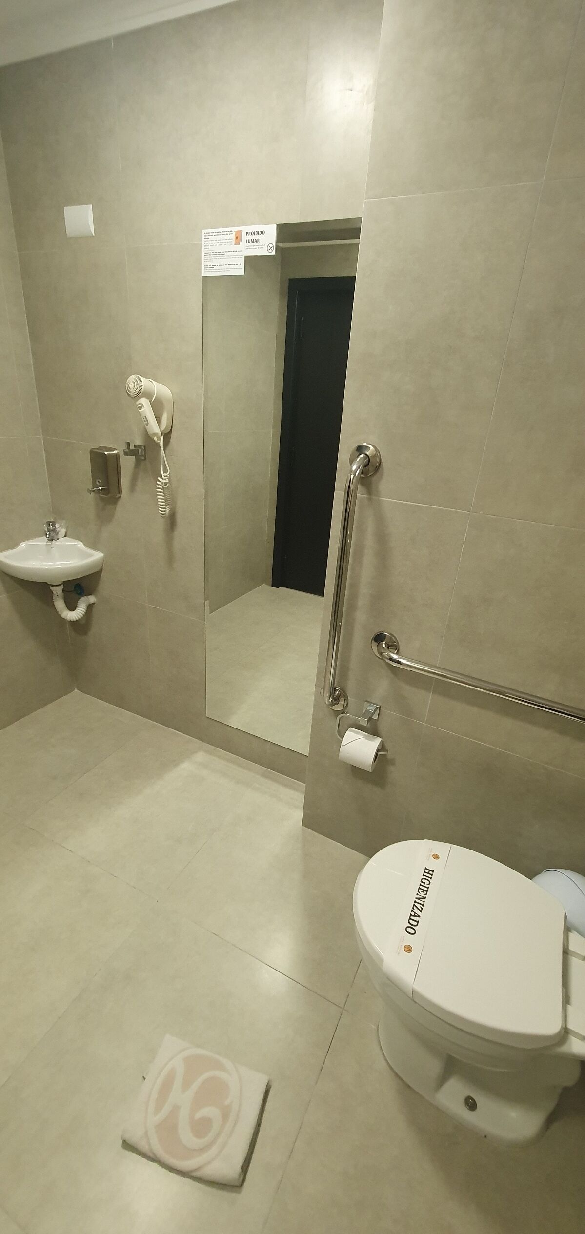 Une salle de bain équipée d’un lavabo, de toilettes, d’un sèche-cheveux et d’une barre d’appui.