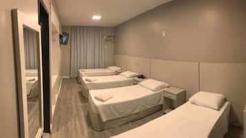 Habitación de hotel con cuatro camas individuales, una mesita de noche con lámpara, un espejo y una ventana con cortinas.
