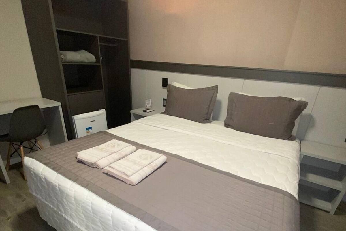 A hotel room with a large bed, a desk, a wardrobe, and a nightstand.