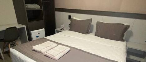 A hotel room with a large bed, a desk, a wardrobe, and a nightstand.