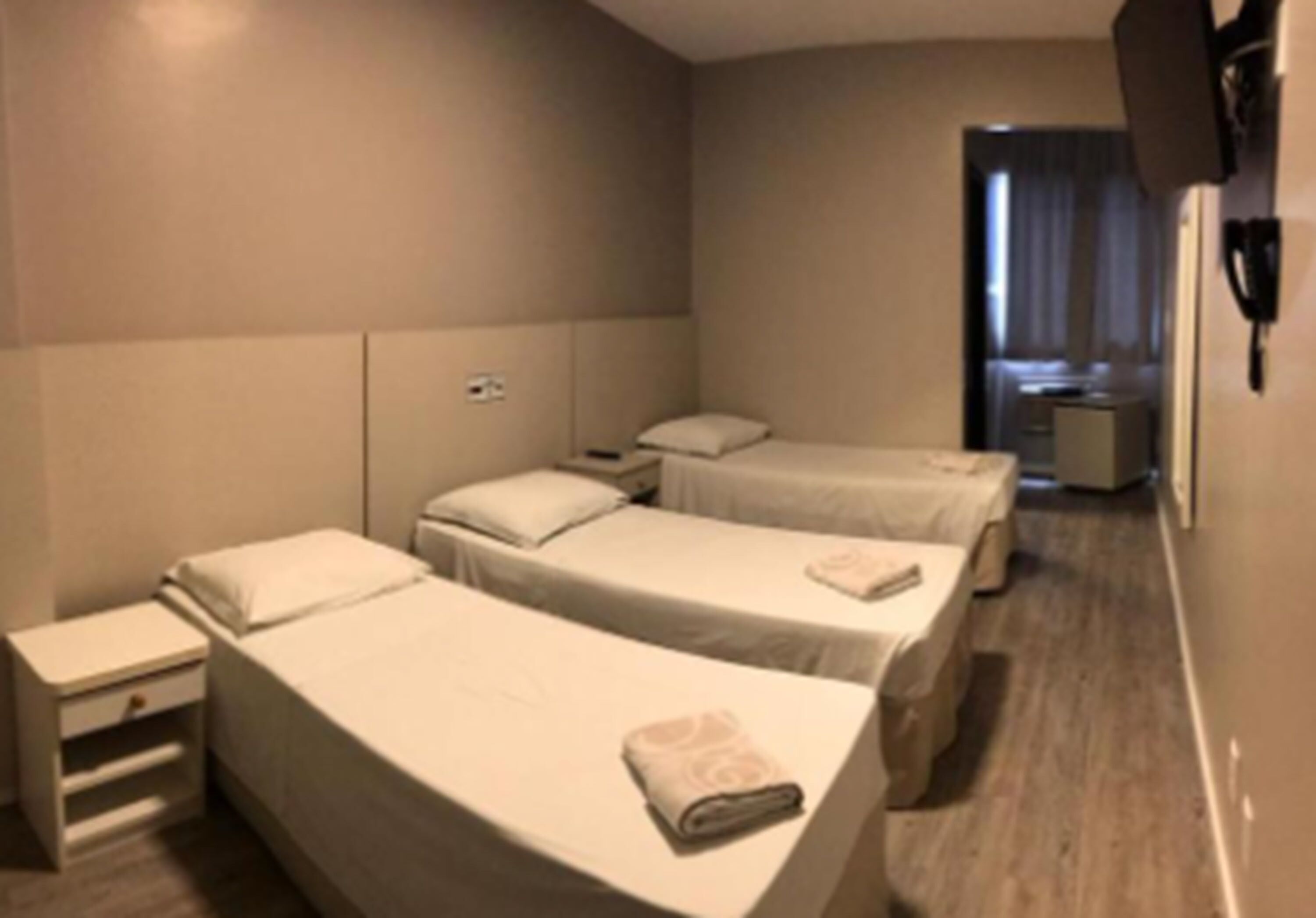 A hotel room with two single beds, a bedside table, a nightstand, and a small desk with a chair.