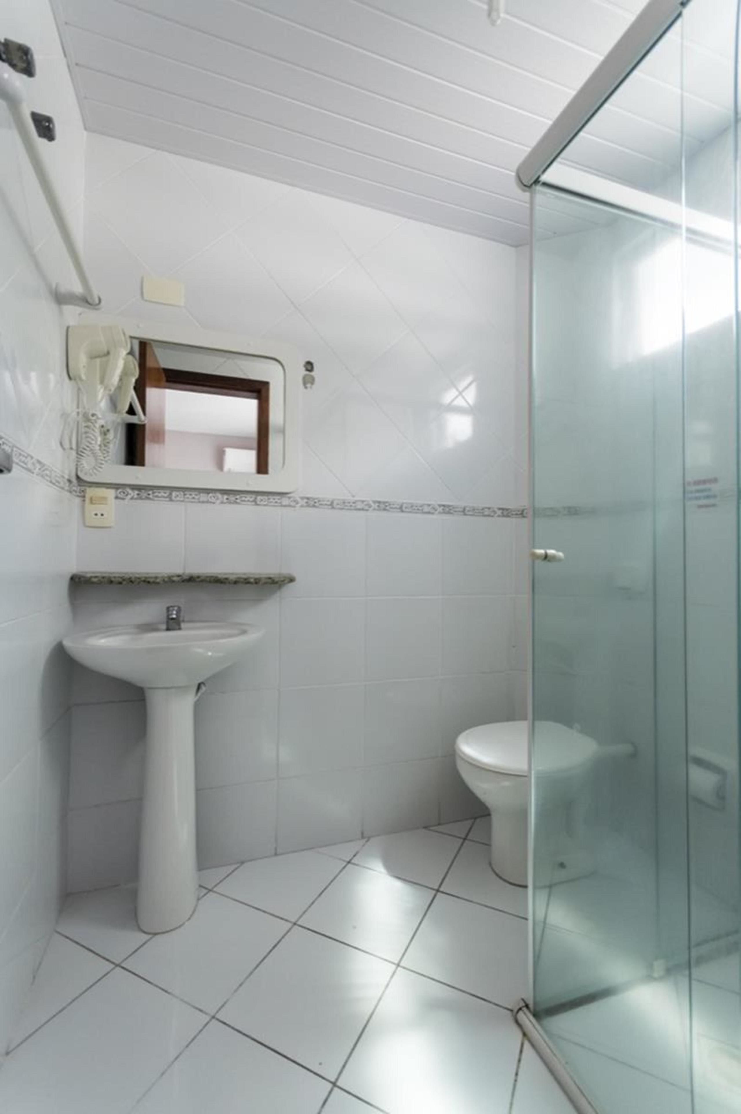 Un baño con cabina de ducha de vidrio, un lavabo pedestal y un inodoro.
