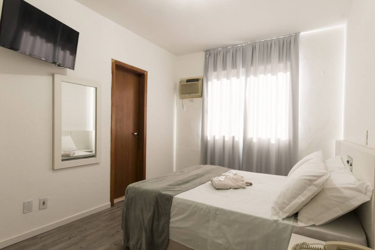 A bedroom with a bed, a mirror, a door, and a window with curtains.