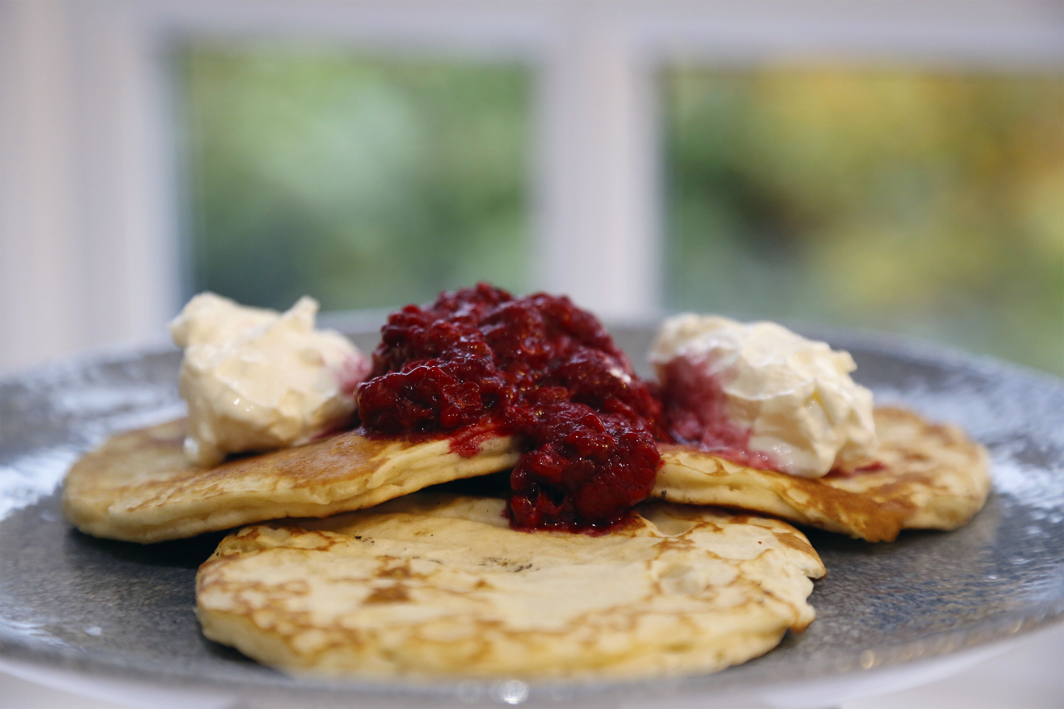 Une assiette de crêpes garnies de compote de fruits rouges et de crème fouettée.