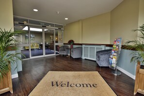 A reception area with a 'Welcome' mat, a magazine rack, and a seating area with chairs and a table. - Quorn Grange Hotel (Loughborough)