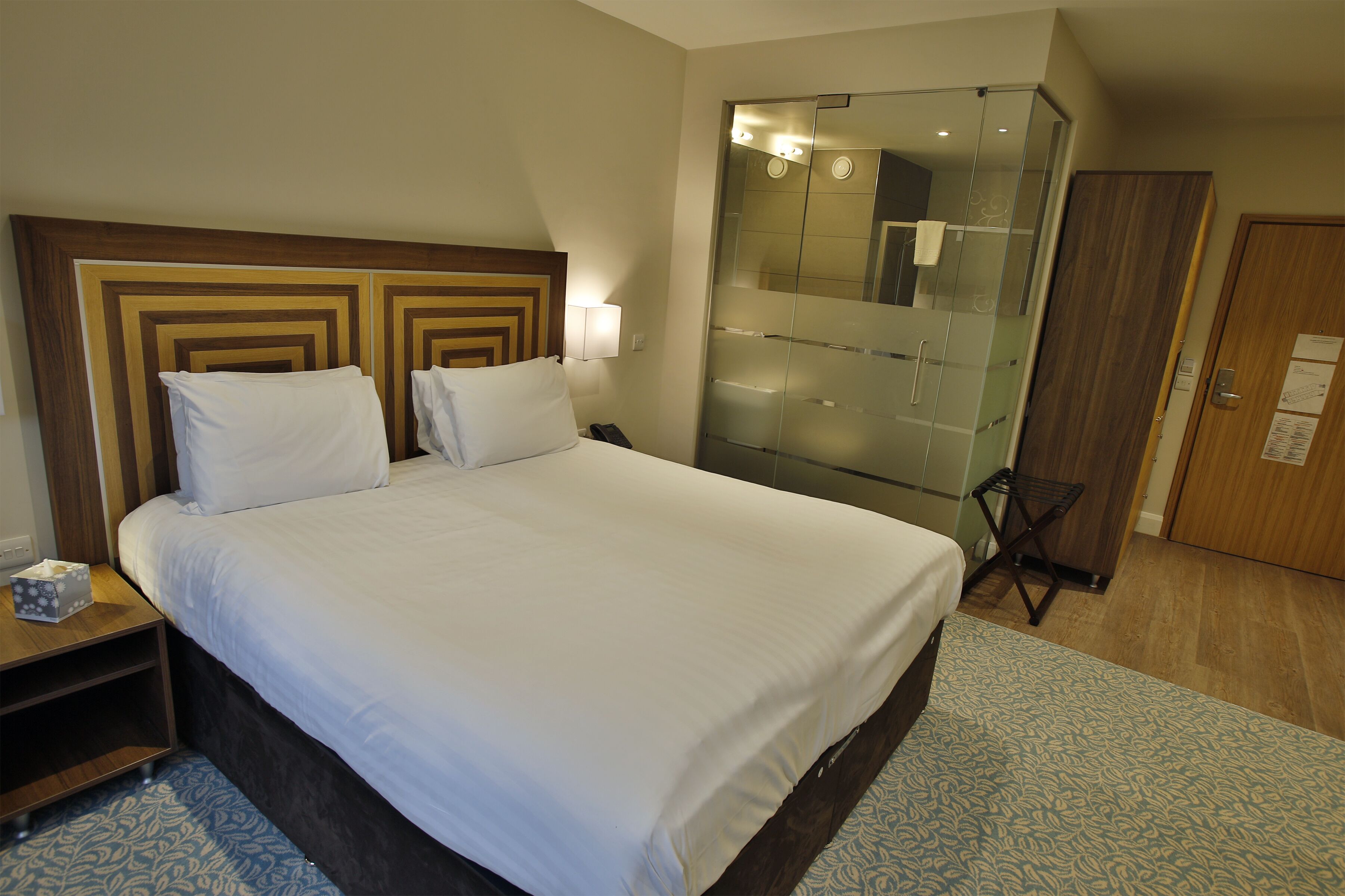 A hotel room with a large bed, a bedside table, a mirror, and a wardrobe.