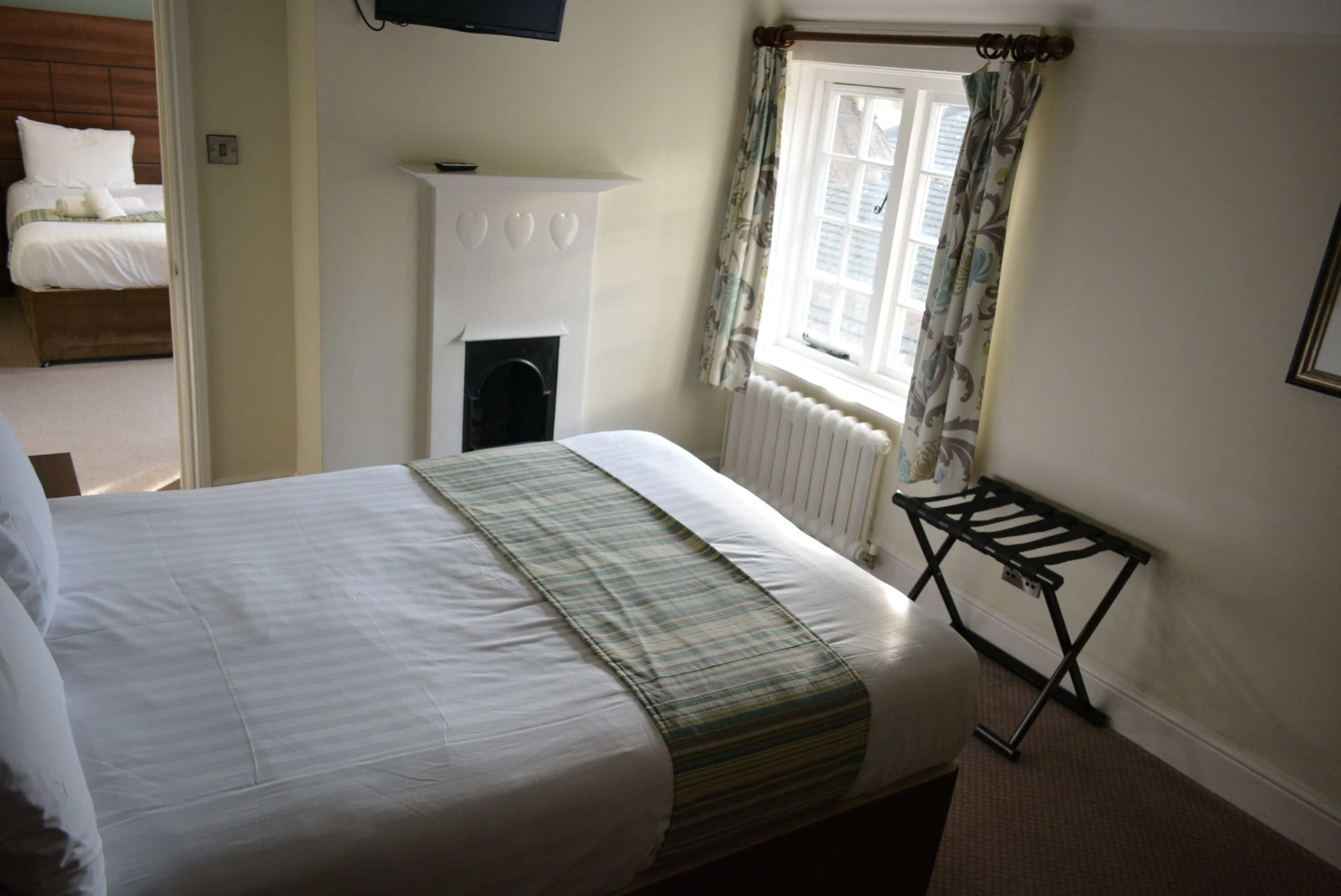 A bedroom with a bed, a radiator, a window with curtains, and a wall-mounted television.