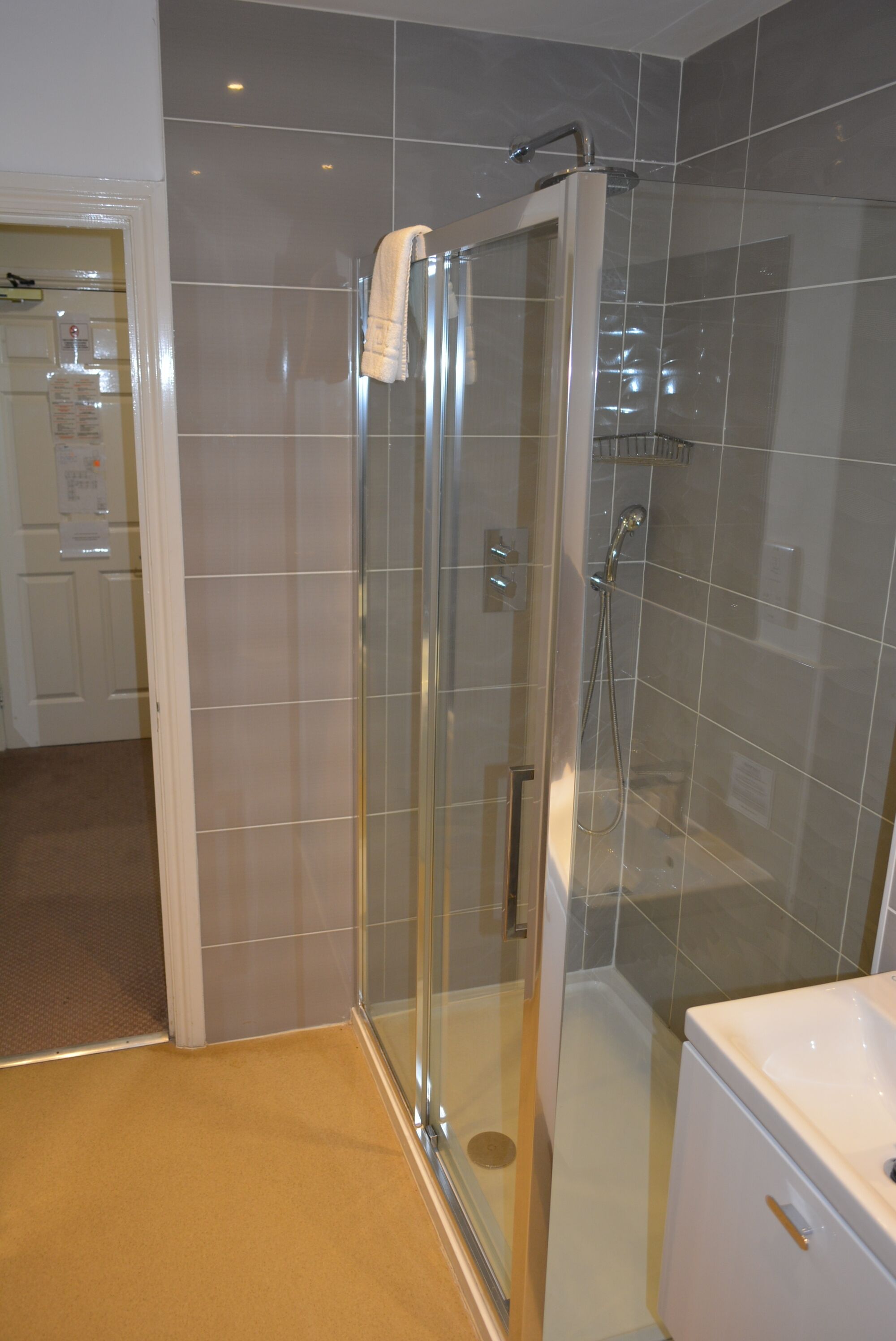 Un baño con ducha vidriada, un lavamanos blanco y piso color beige.