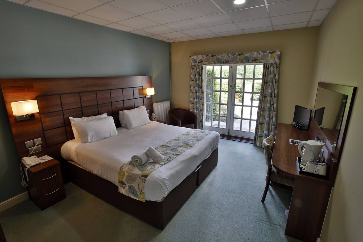 A hotel room with a large bed, bedside lamps, a desk with a computer, and a window with curtains.