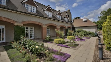 A building with a brick facade, multiple windows, and a paved courtyard with flower beds.