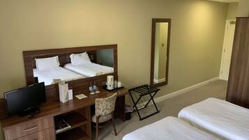 A hotel room with a bed, a desk with a computer, a chair, a coffee maker, and a mirror.
