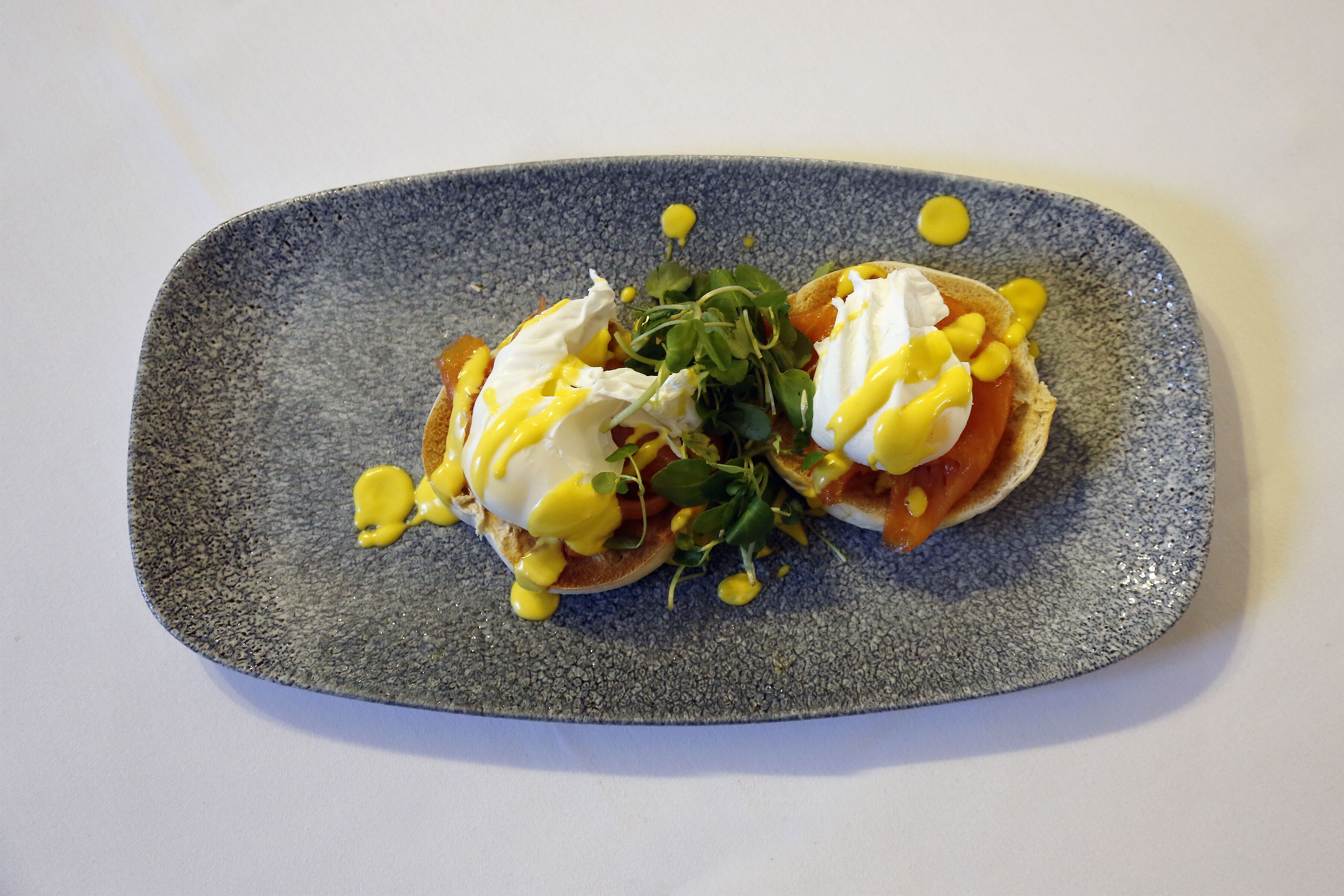 Kaksi uppopaistettua kananmunaa paahtoleivän päällä, tarjoiltuna hollandaise-kastikkeen ja vihreiden salaattien kera, ja kaikki on aseteltu kuvioiduille lautasille.