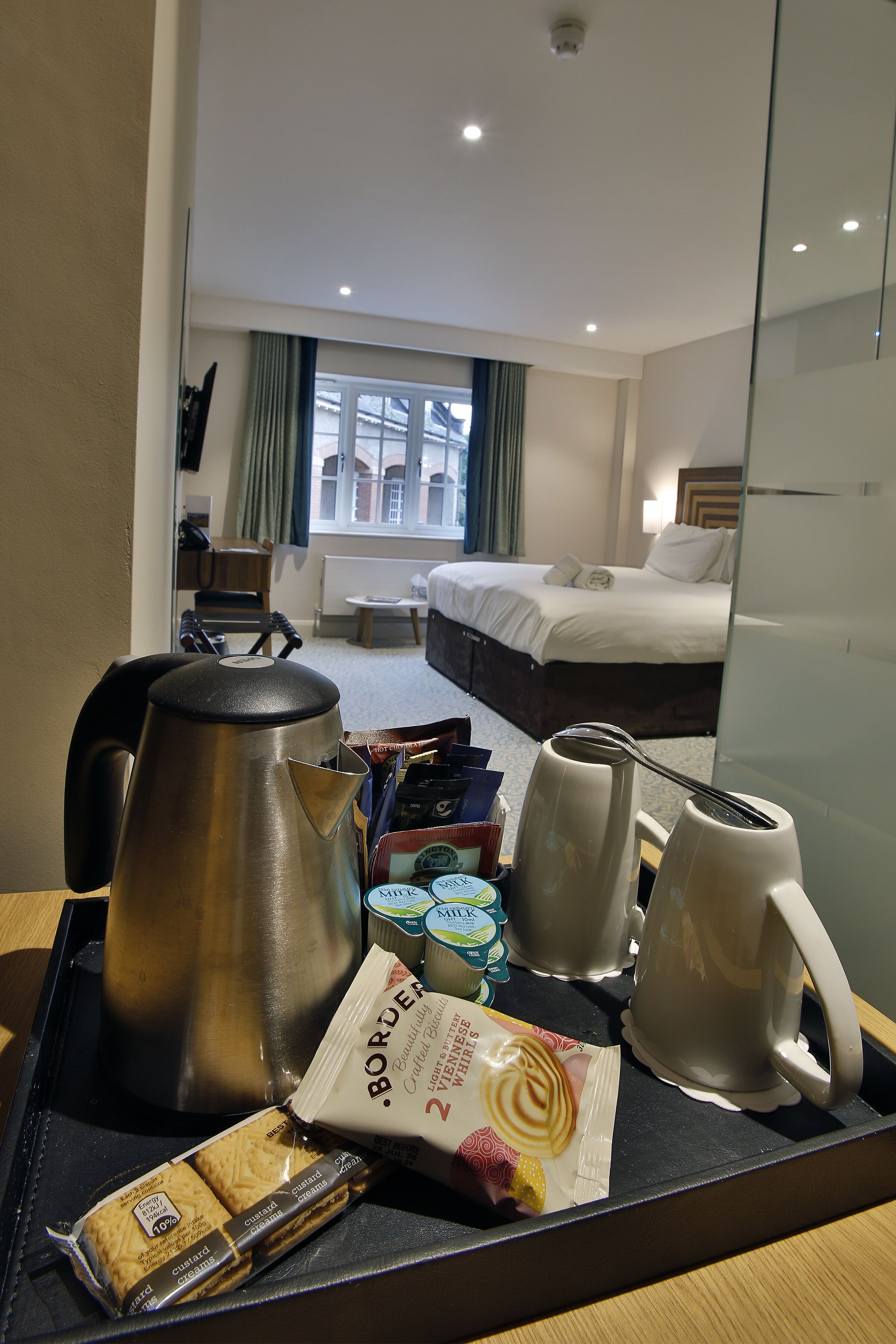 Una habitación de hotel con una cama, un escritorio con hervidor, tazas y aperitivos.