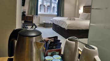 A hotel room with a bed, a desk with a kettle, cups, and snacks.