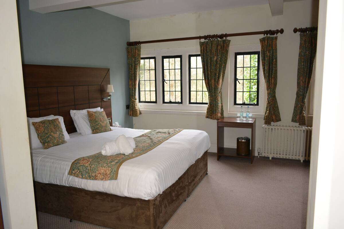 A neatly made bed with a wooden headboard, a bedside table with a lamp, and a window with curtains.