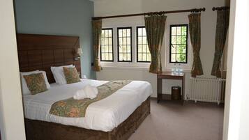 A neatly made bed with a wooden headboard, a bedside table with a lamp, and a window with curtains.