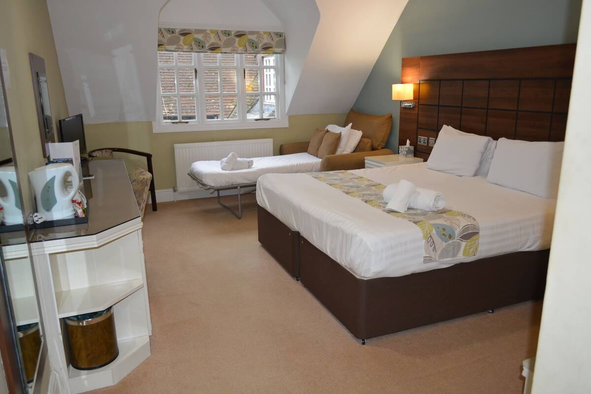 A hotel room with a large bed, a desk with a computer, a chair, and a window with a view of buildings.