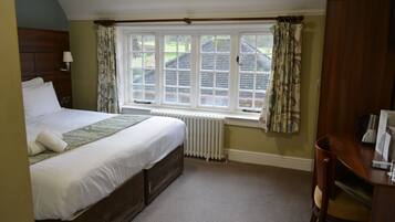 A bedroom with a bed, a window with curtains, a radiator, and a desk with a chair.