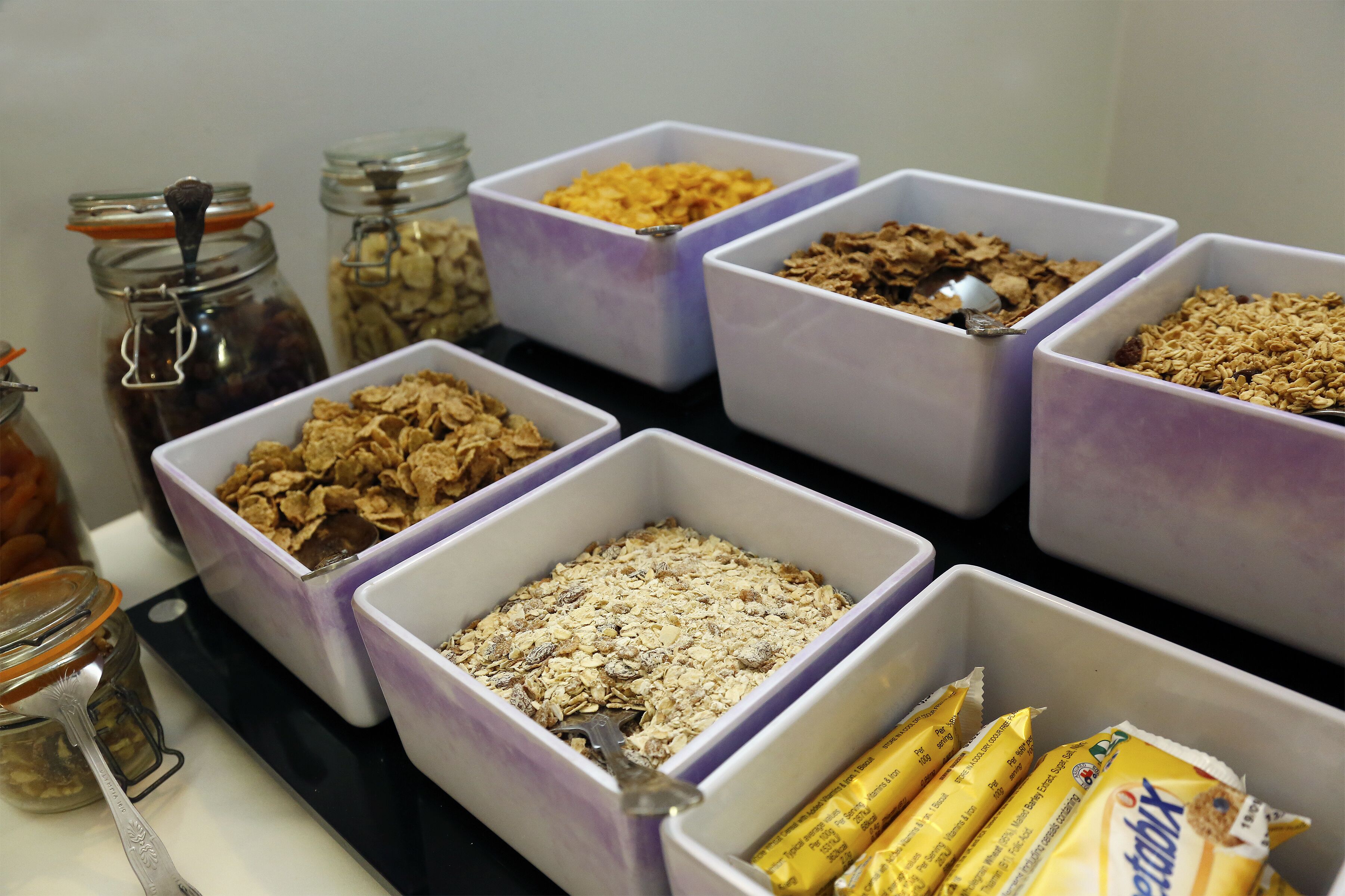 Multiple containers with various food items, including cereals and snacks, arranged on a table.