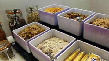 Meerdere bakken met verschillende etenswaren, zoals ontbijtgranen en snacks, op een tafel gerangschikt.
