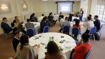 A conference room with round tables, attendees seated, and a presentation screen.