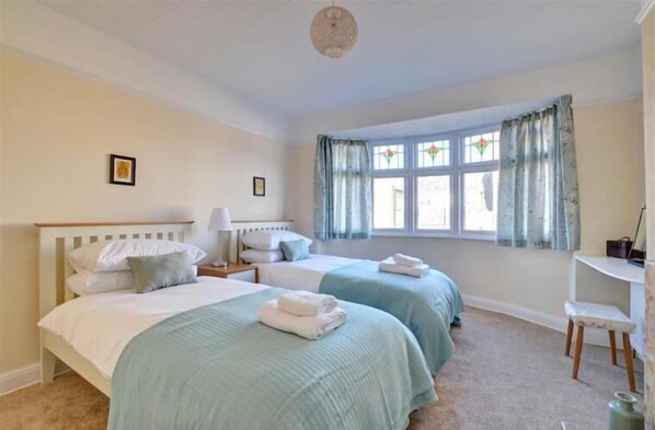 A bedroom with two beds, a desk, and a window with curtains.