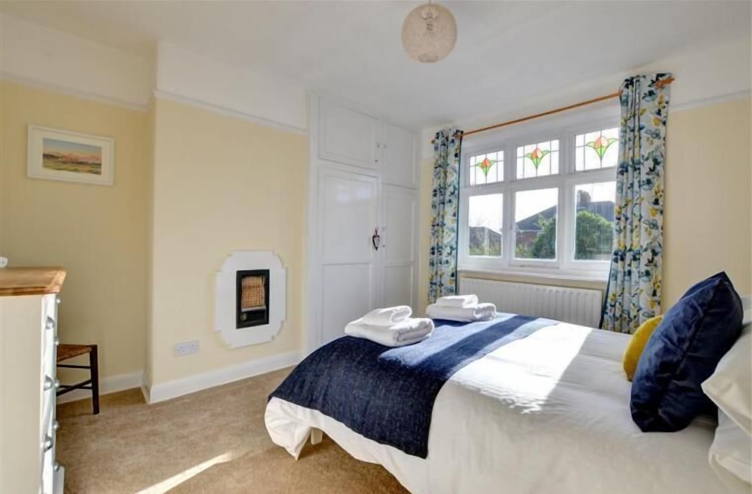 A bedroom with a bed, a window with curtains, a radiator, and a picture on the wall.