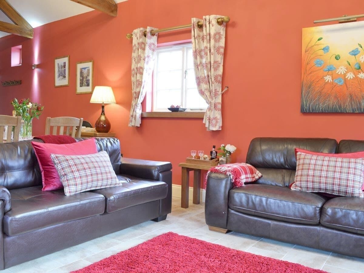 A living room with two leather sofas, a red rug, a small table with drinks, and a window with curtains.