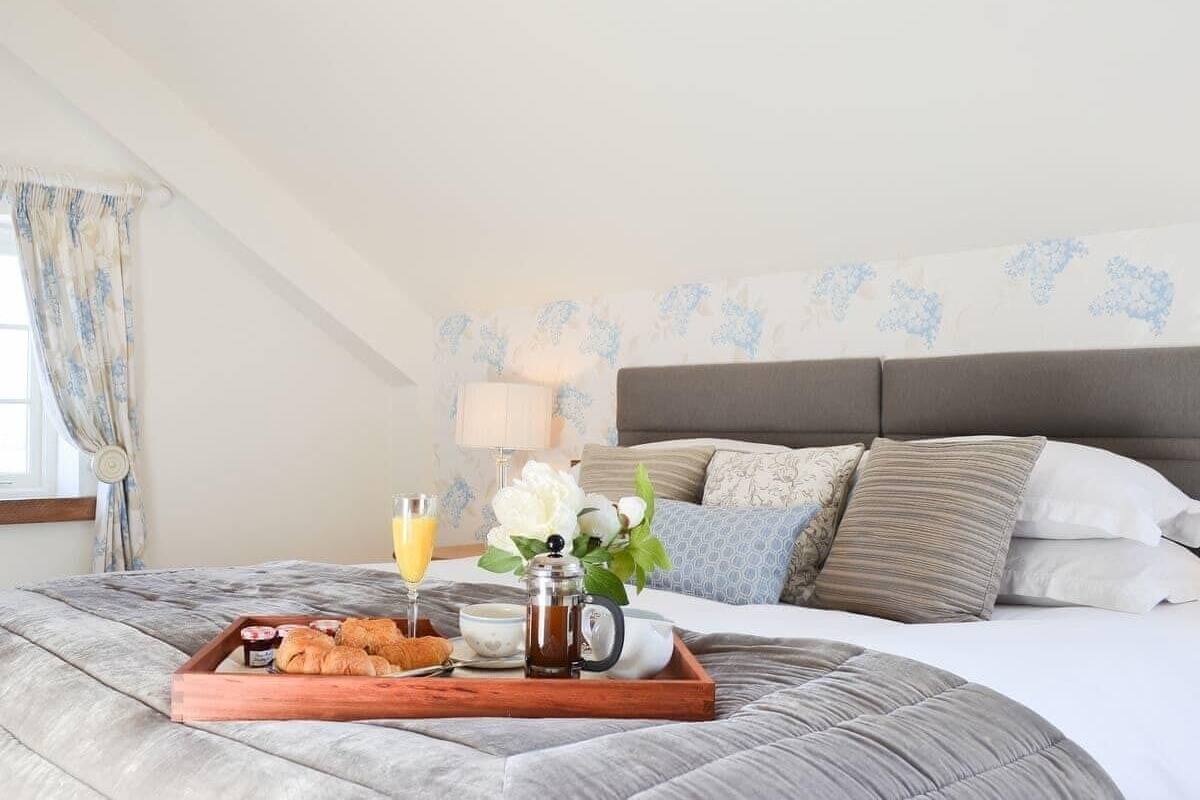 A neatly made bed with a tray of breakfast items, including croissants, a coffee pot, and a glass of orange juice.
