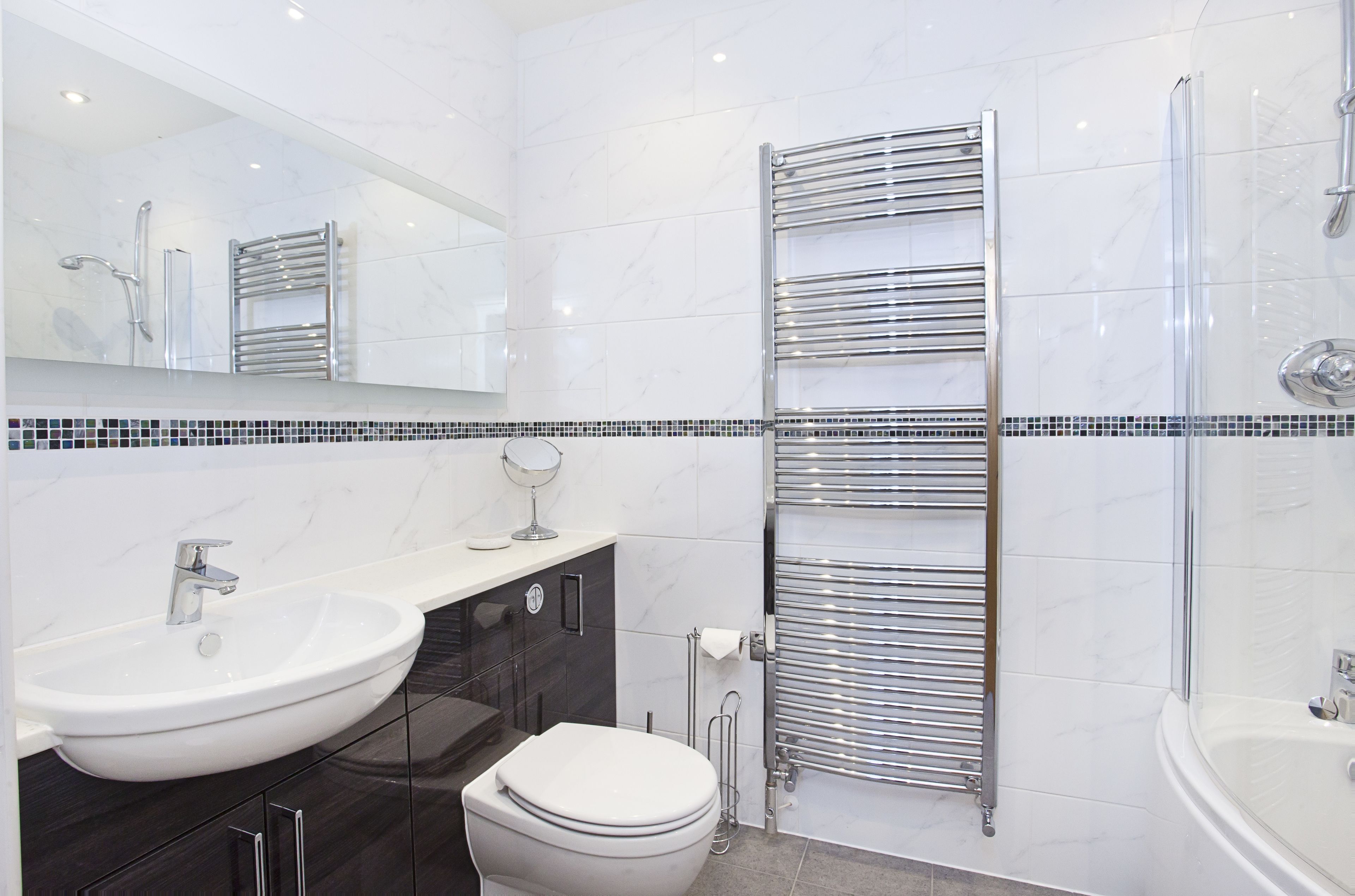 Une salle de bain moderne avec un lavabo blanc, des toilettes, un grand miroir et une douche à parois de verre.
