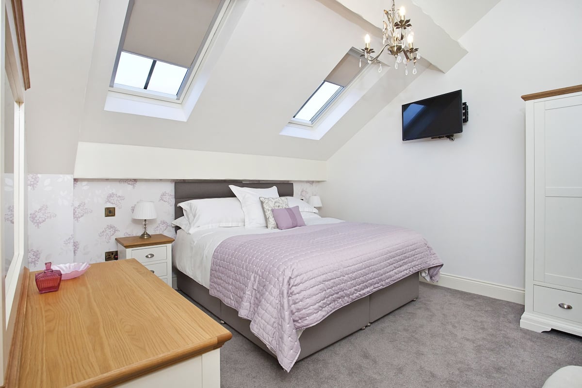 A bedroom with a bed, a desk, a TV, and a wardrobe.
