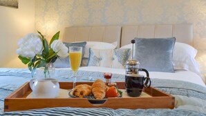 A neatly made breakfast tray with croissants, fruit, and a coffee pot on a bed with a patterned headboard. - Holtby Grange Cottages (York)