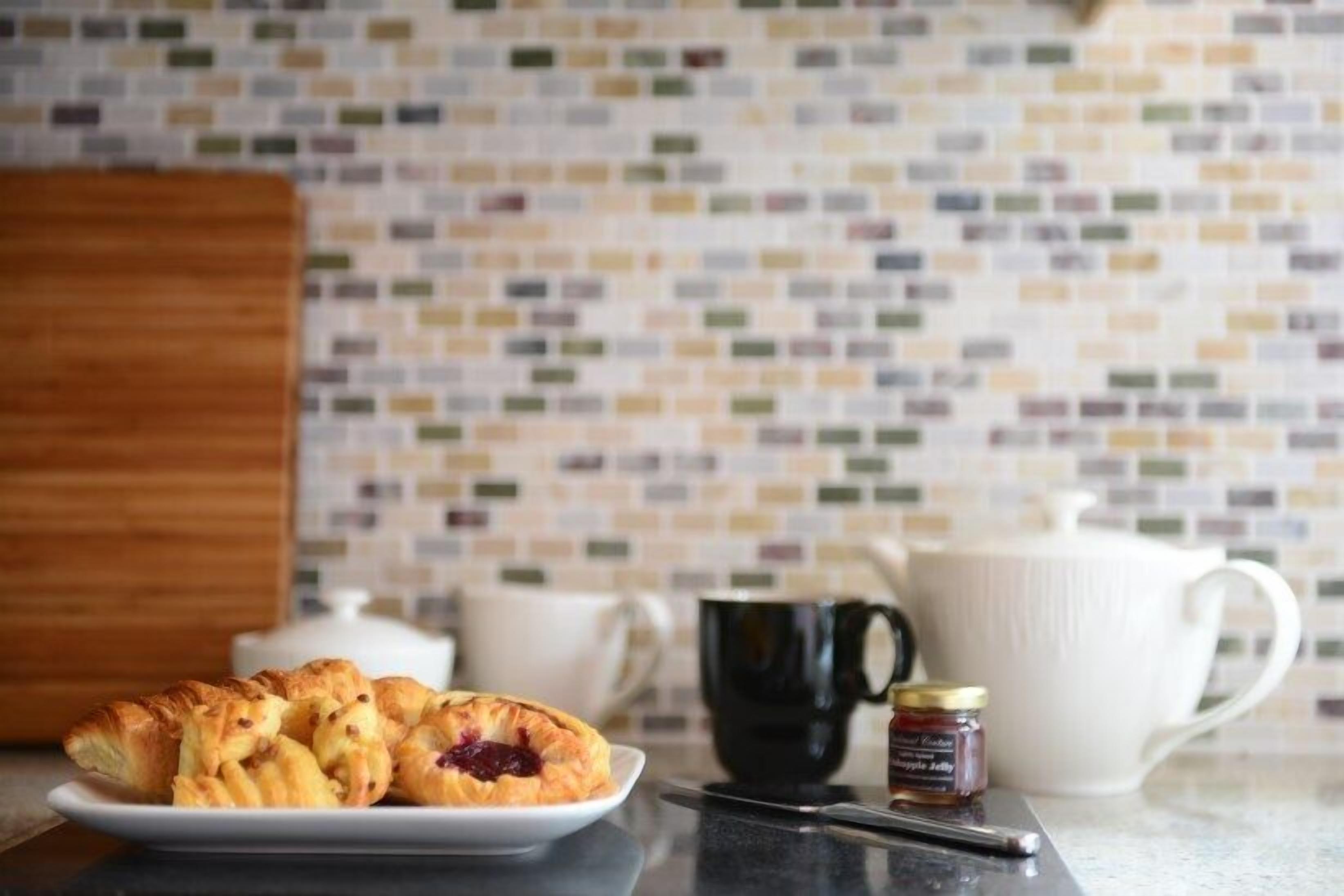 A breakfast setting with pastries on a plate, a black mug, a white teapot, and a jar of jam.