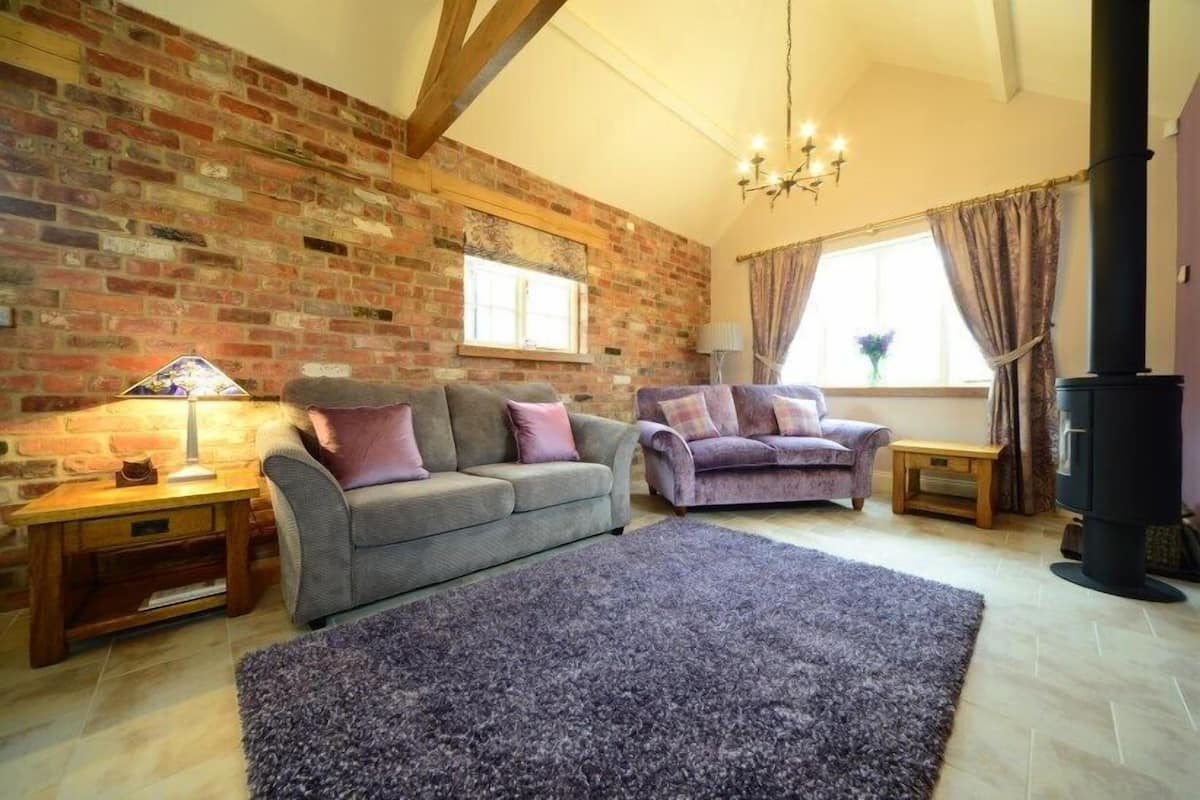 A cozy living room with a brick wall, two sofas, a large rug, and a fireplace.