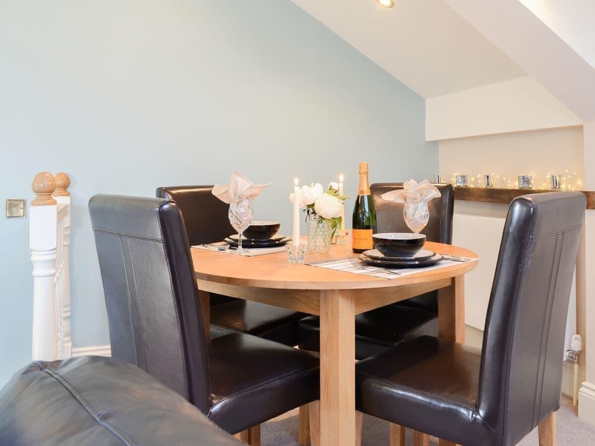 A dining table with four black leather chairs, a bottle of champagne, candles, and a vase with flowers.