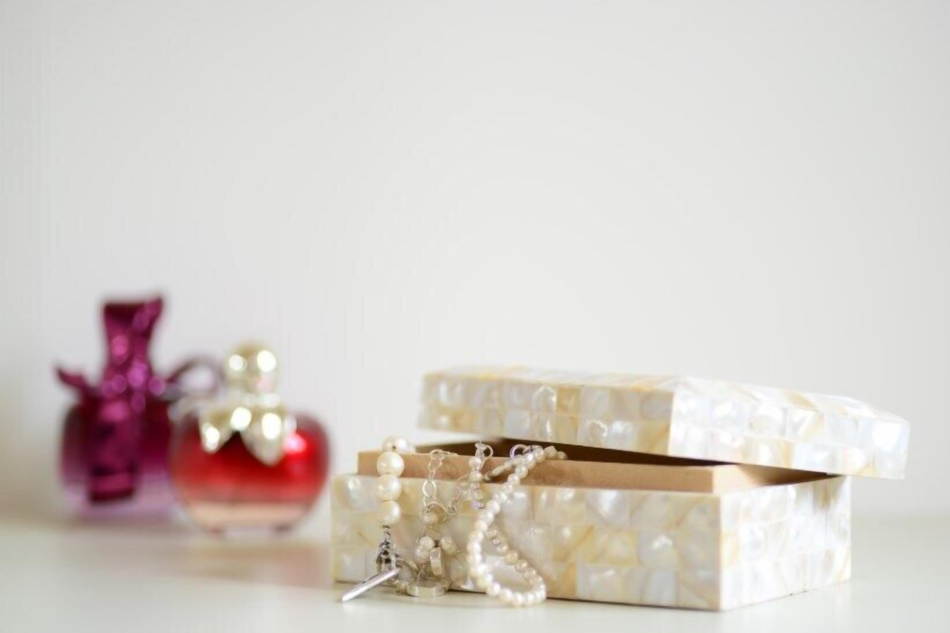A small, open jewelry box with a pearl necklace and a keychain, and a red perfume bottle in the background.