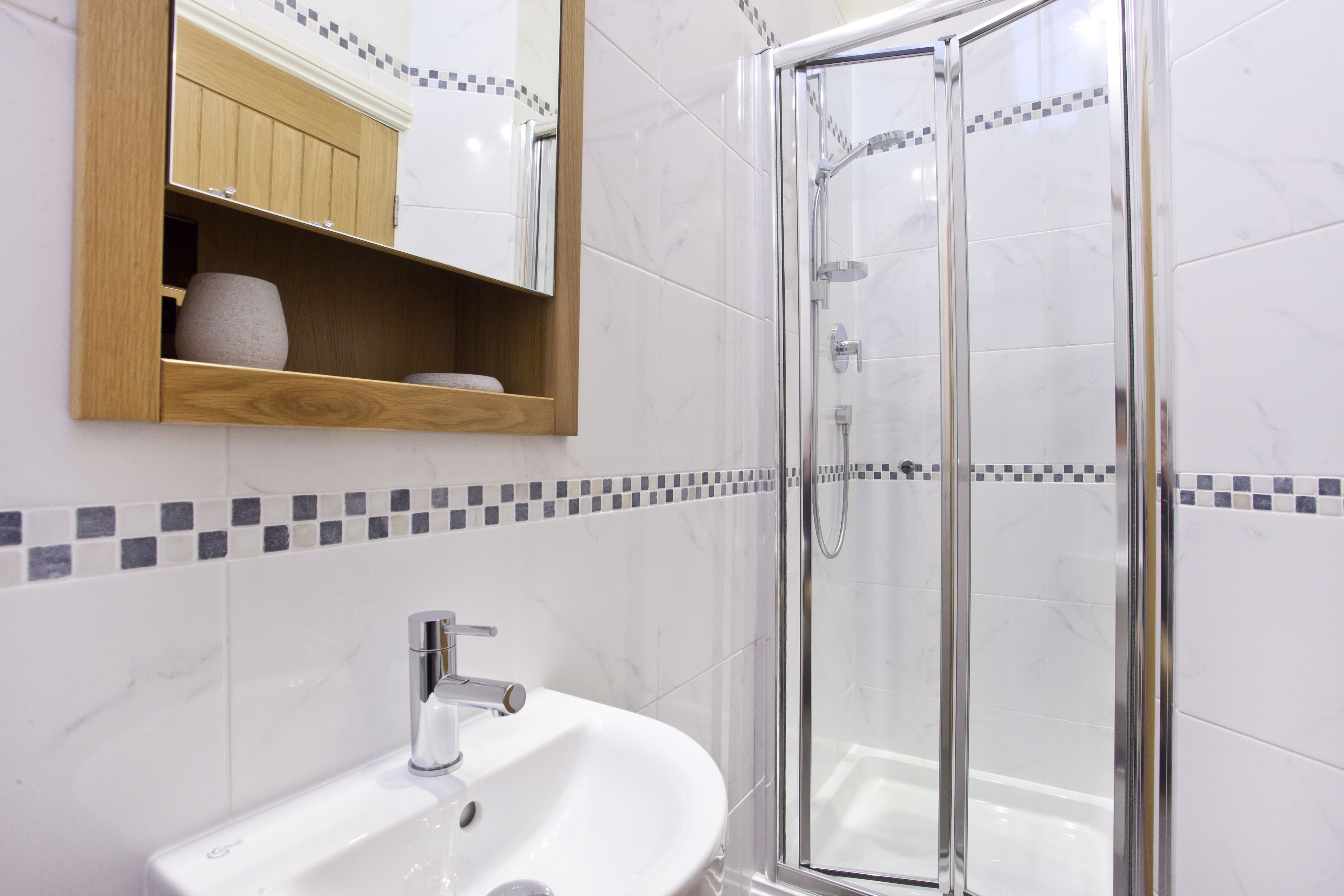 A bathroom with a white sink, a wooden medicine cabinet, and a glass shower enclosure.
