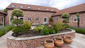 A brick building with a courtyard, potted plants, and a patio area. - Holtby Grange Cottages (York)
